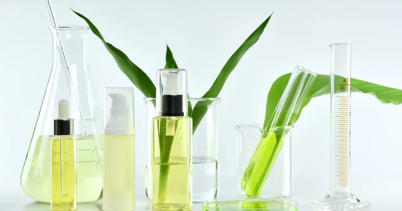 Laboratorium kosmetyczne bada, co to są parabeny. Widać tam buteleczki z kosmetykami, zieleń roślin i szkło laboratoryjne.