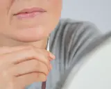Dłoń z pęsetą usuwa delikatny meszek na twarzy pod brodą.