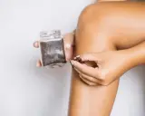 Dłoń nabiera drobny peeling cukrowy z słoiczka, by wykonać domowy zabieg pielęgnacyjny.