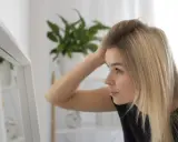 Kobieta z blond włosami poprawia fryzurę przed lustrem, zastanawiając się, sls co to jest i jak wpływa na jej wygląd.