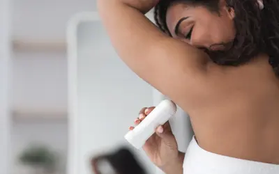 Kobieta aplikuje biały antyperspirant pod pachę, pokazując, jak działa antyperspirant, by czuć się świeżo przez cały dzień.