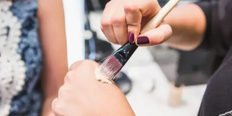 Dłoń z ciemnym lakierem do paznokci nabiera krem BB na pędzel, by nałożyć go na drugą dłoń.