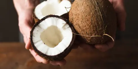 Dłonie trzymają połówki kokosa. Olej kokosowy na co pomaga? Na zdrowie i urodę!