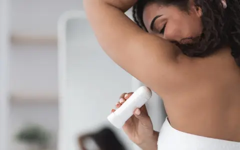 Kobieta aplikuje biały antyperspirant pod pachę, pokazując, jak działa antyperspirant, by czuć się świeżo przez cały dzień.