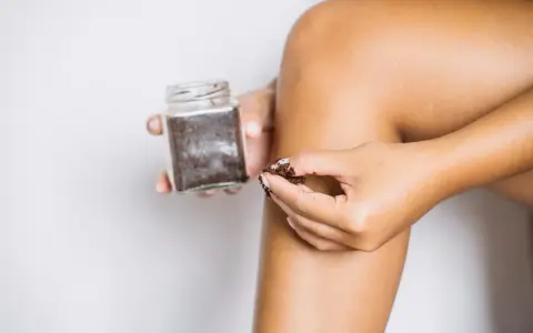 Dłoń nabiera drobny peeling cukrowy z słoiczka, by wykonać domowy zabieg pielęgnacyjny.