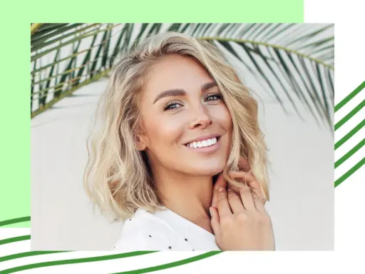 Uśmiechnięta blondynka z falowanymi, cienkimi włosami w stylu long bob, na tle liści palmy.