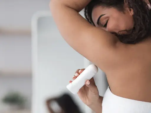 Kobieta aplikuje biały antyperspirant pod pachę, pokazując, jak działa antyperspirant, by czuć się świeżo przez cały dzień.