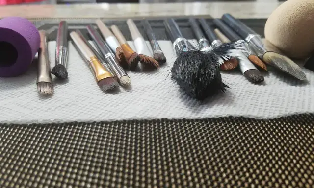 Pędzle do makijażu leżą na ręczniku papierowym, gotowe do mycia. Widać różne rodzaje pędzli, od małych po większe, z różnymi końcówkami.