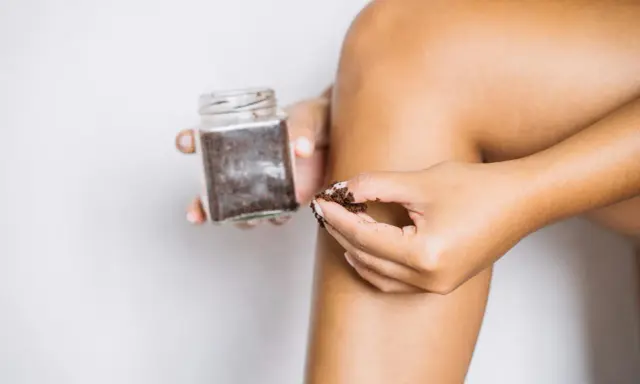 Dłoń nabiera drobny peeling cukrowy z słoiczka, by wykonać domowy zabieg pielęgnacyjny.