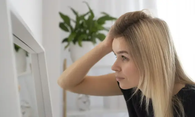 Kobieta z blond włosami poprawia fryzurę przed lustrem, zastanawiając się, sls co to jest i jak wpływa na jej wygląd.