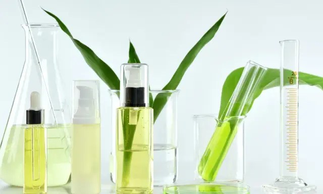Laboratorium kosmetyczne bada, co to są parabeny. Widać tam buteleczki z kosmetykami, zieleń roślin i szkło laboratoryjne.