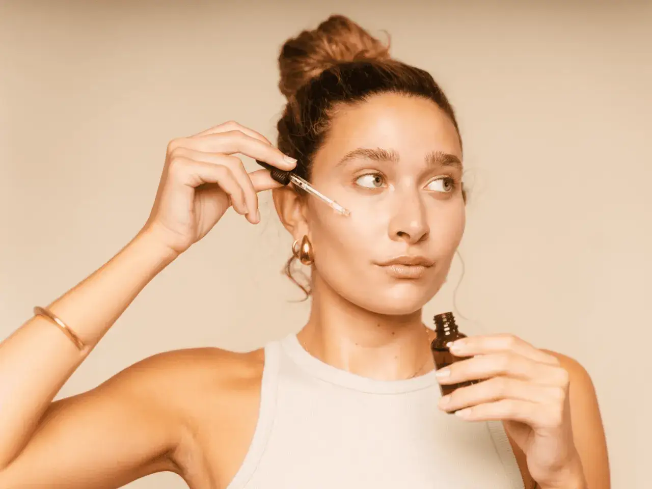Kobieta aplikuje serum na twarz, przygotowując skórę do makijażu. Idealna pielęgnacja pod makijaż dla promiennej cery.